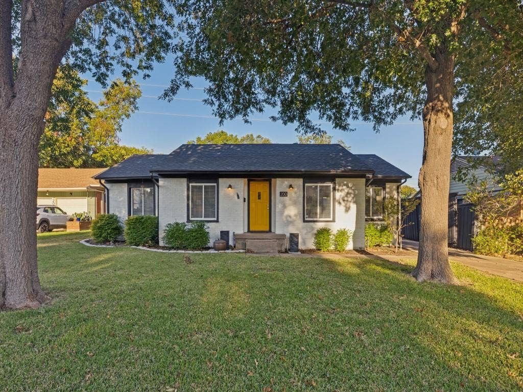 200 S Weatherred Drive, Richardson, TX 75080 Single-story residence featuring a painted masonry exterior, shingle roof, contrasting window trim, and a prominent yellow entry door, situated on a lot with mature shade trees