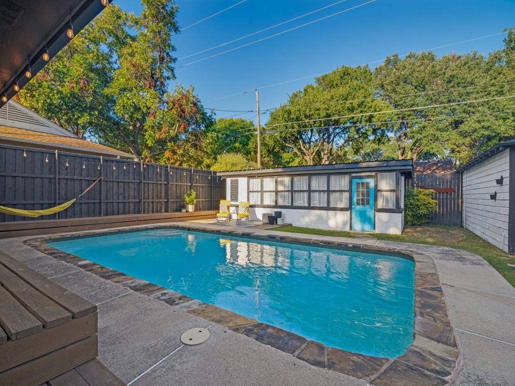 200 S Weatherred Drive, Richardson, TX 75080 Outdoor area featuring an in-ground swimming pool, stone-trimmed concrete decking, a wood-surround pool deck, a detached structure with multi-pane windows, and a privacy fence