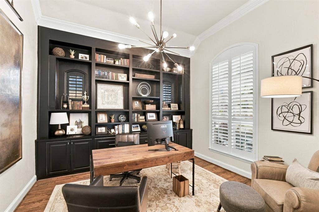 Custom floor-to-ceiling built-in cabinetry, arched window with plantation shutters, crown molding, and modern multi-arm chandelier