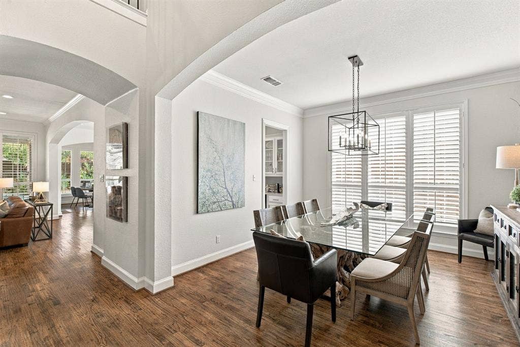 Wood-finish flooring, architectural archways, crown molding, plantation shutters, and a geometric metal chandelier