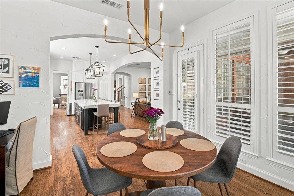 Dining area featuring wood-finish flooring, an arched entryway, and tall windows with plantation shutters, accented by a multi-arm metallic chandelier