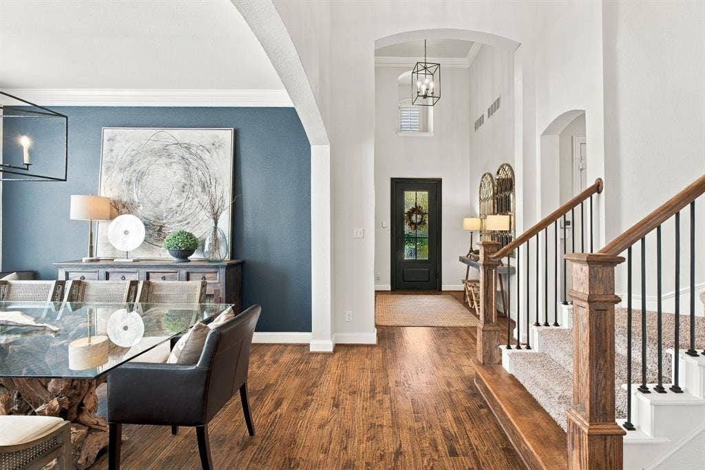 Foyer and dining area featuring wood-finish flooring, high ceilings with archway detailing, a multi-pane glass entry door, and a staircase with a wood handrail and iron balusters