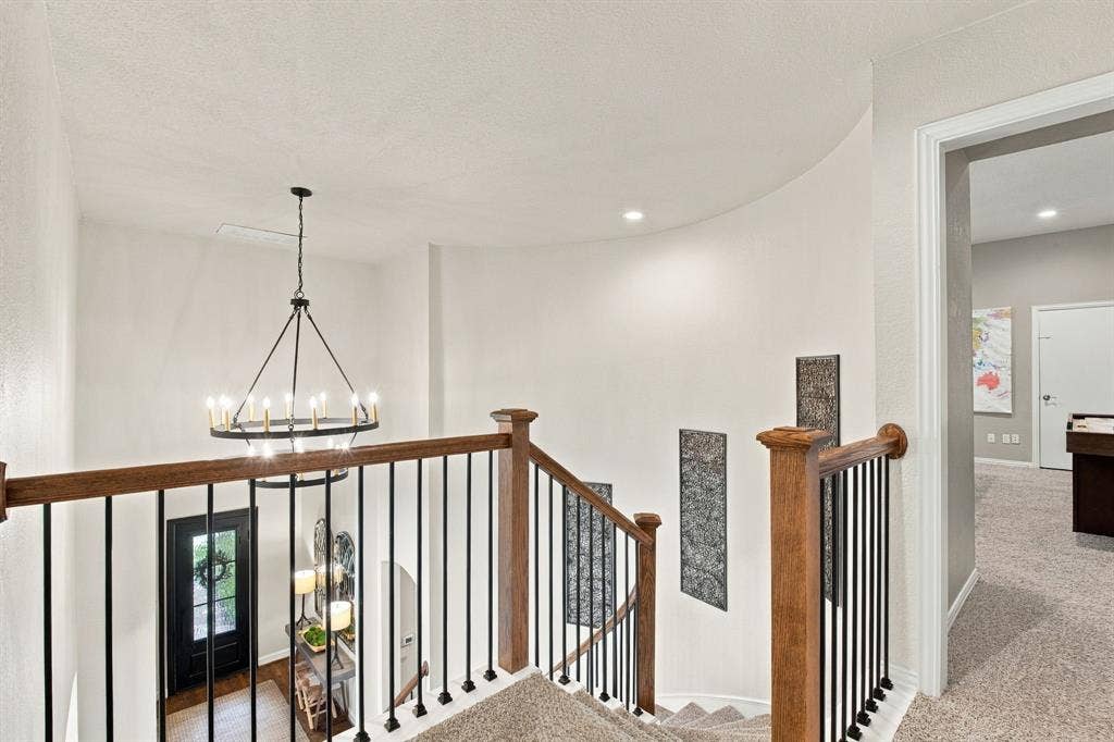 Curved wall design featuring a staircase with wood-finish railing, metal balusters, and a tiered chandelier