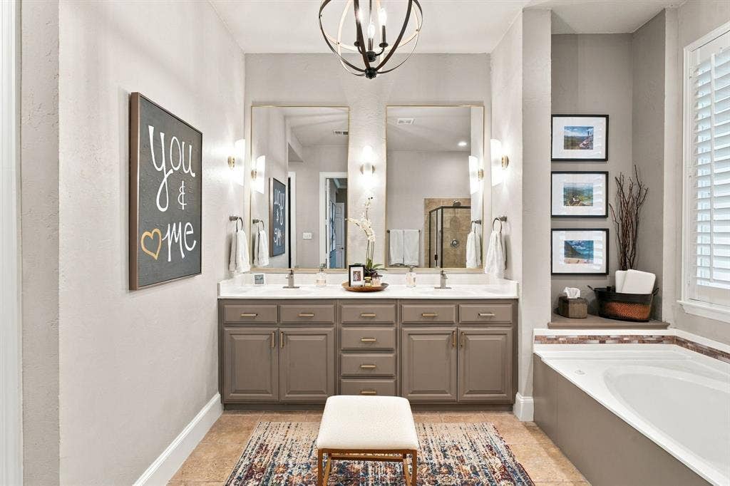 Double vanity with light-toned countertops, shaker-style cabinetry, dual rectangular mirrors, and a deep soaking tub featuring tile surrounds