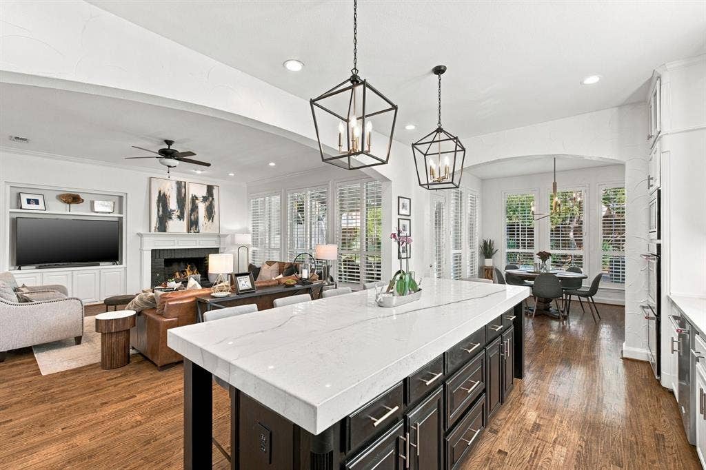 Kitchen island featuring a stone-look countertop and dark cabinetry, wood-finish flooring, geometric pendant lighting, and a built-in media center with a fireplace