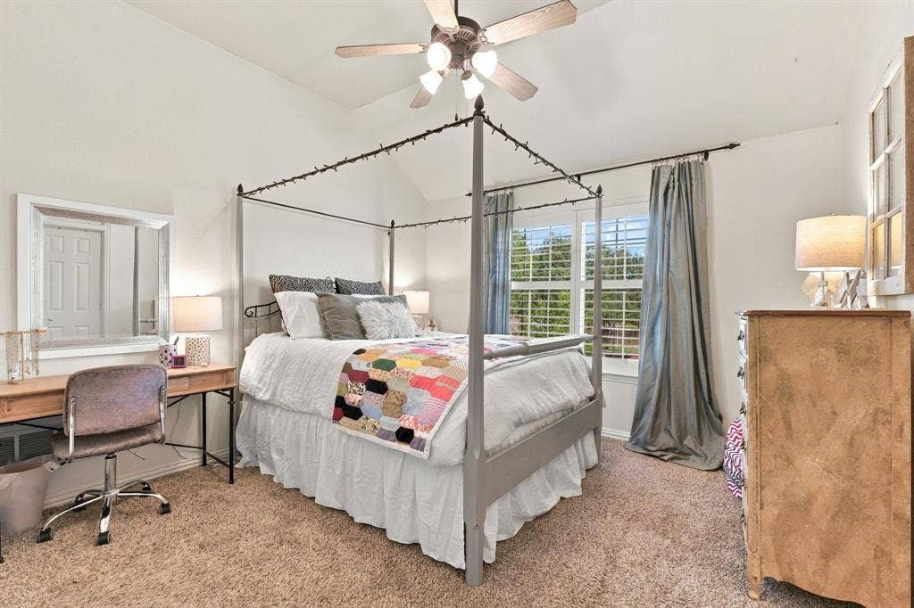 Vaulted ceiling room featuring neutral carpeting, multi-pane windows with grid mullions, and a central ceiling fan with integrated light fixture