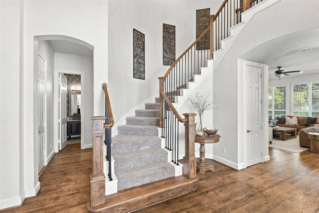Foyer featuring wood-finish flooring, staircase with carpeted treads, wood handrails, and vertical metal balusters