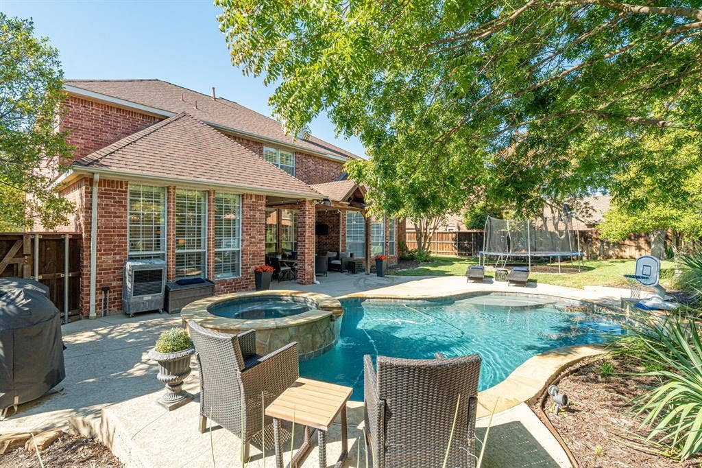 Red brick exterior featuring a multi-level roofline, swimming pool with a raised stone-accented spa, covered patio, and manicured lawn
