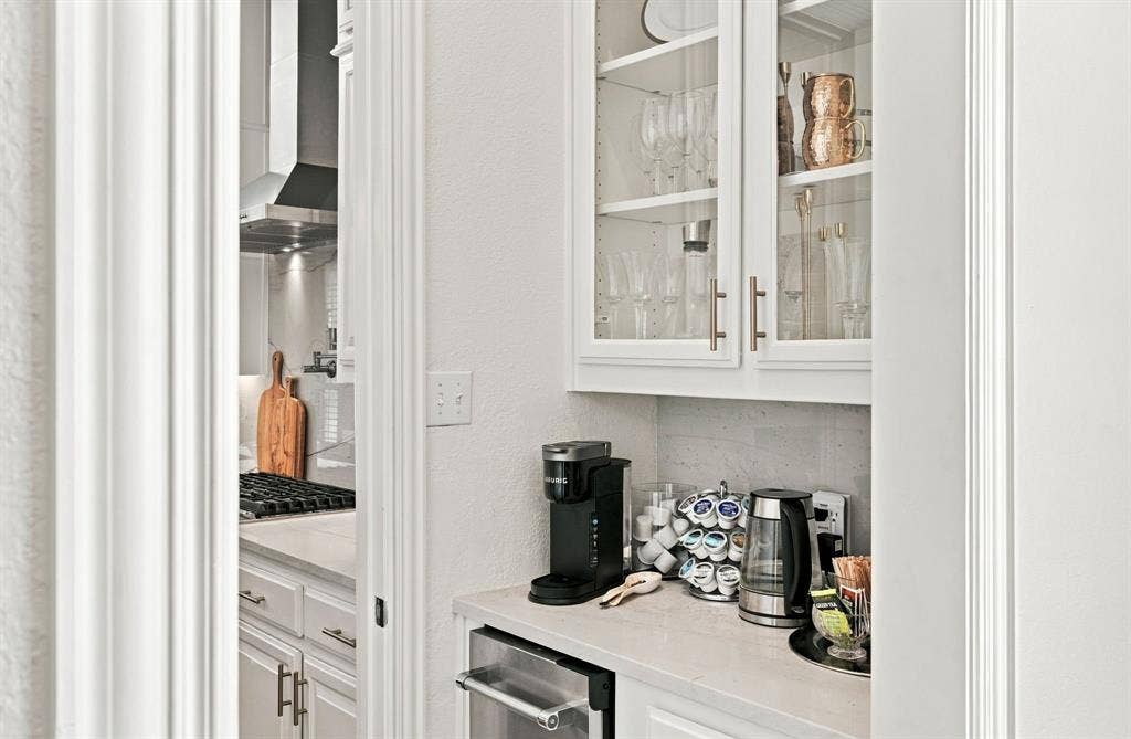 White cabinetry with glass-panel upper doors, stone-finish countertops, stainless steel under-counter appliance, and stone-tiled backsplash