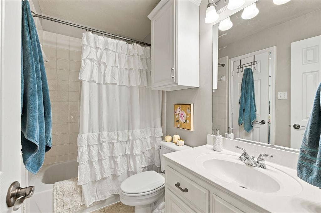 Bathroom featuring a white vanity with an integrated sink, polished chrome faucet, wall-mounted storage cabinet, full-width mirror with overhead light fixture, and a tile-surround bathtub