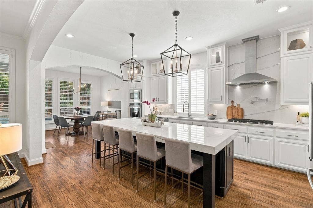 Kitchen featuring a large central island with stone-surface countertop, white cabinetry, integrated stainless steel appliances, geometric pendant lighting, and wood-finish flooring