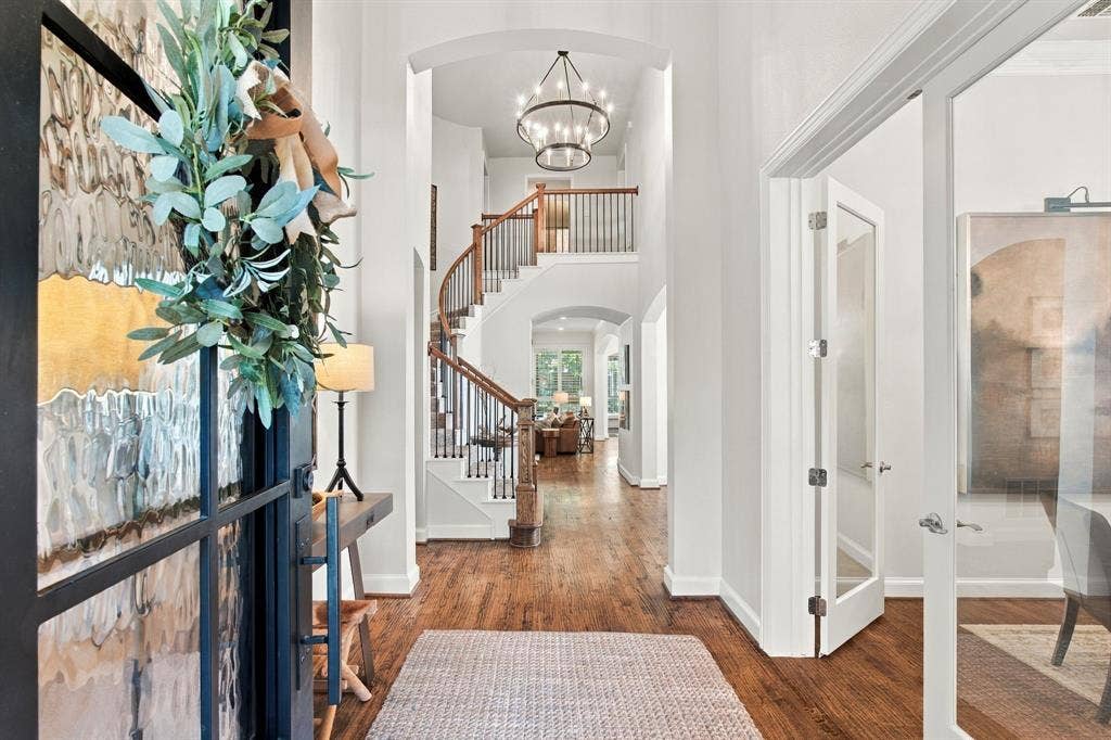 Entryway featuring wood-finish flooring, a curved staircase with a wooden banister, arched openings, a multi-tiered metal chandelier, and a glass-paneled entry door