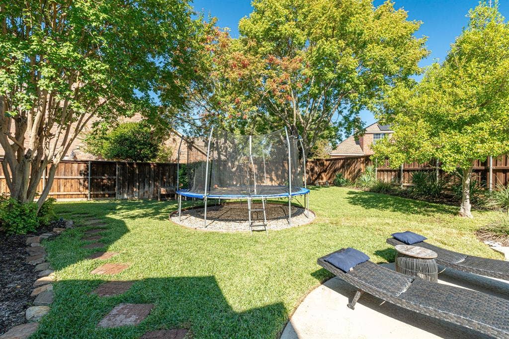 Rear yard featuring a manicured lawn, stone paver pathway, mature trees, wood privacy fencing, and a concrete patio