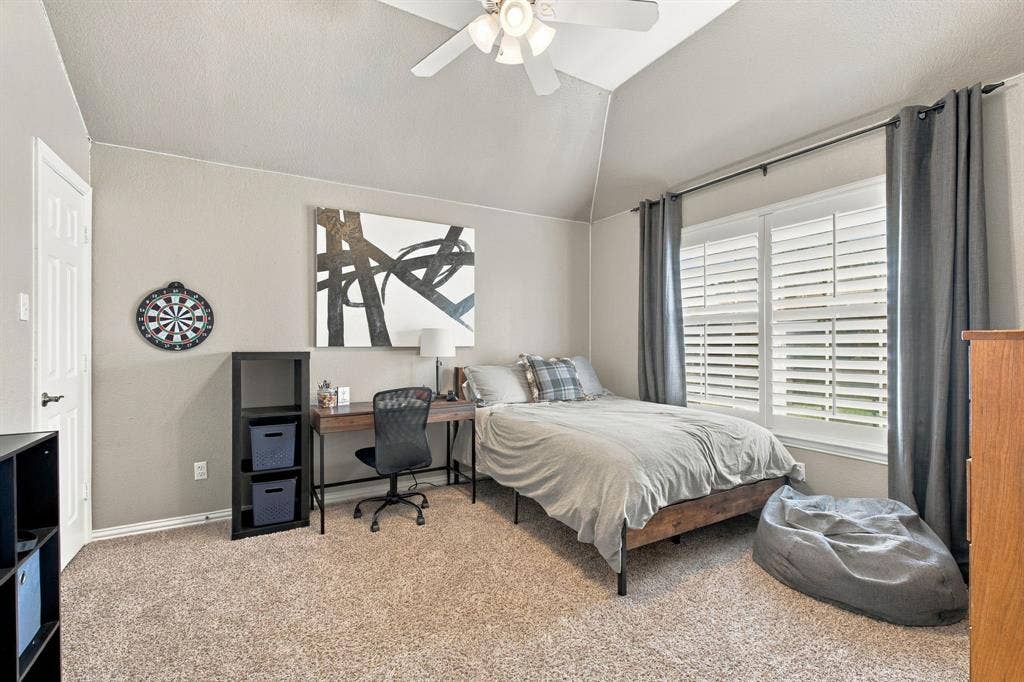 Vaulted ceiling with a central multi-blade ceiling fan, neutral wall tones, plush wall-to-wall carpeting, and interior window shutters