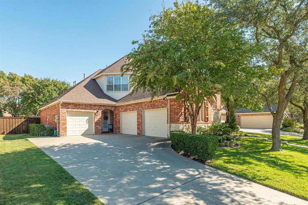 Brick and stone exterior featuring a multi-car garage, pitched shingle roof, and a concrete driveway