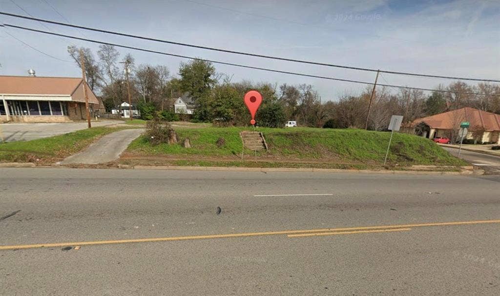 Vacant lot featuring a paved driveway, elevated grass terrain, and concrete steps