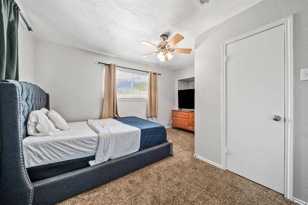 2807 Cain Boulevard, Dallas, TX 75211 Neutral wall paint, textured ceiling, window with exterior scenery, ceiling fan with light fixture, and carpet flooring