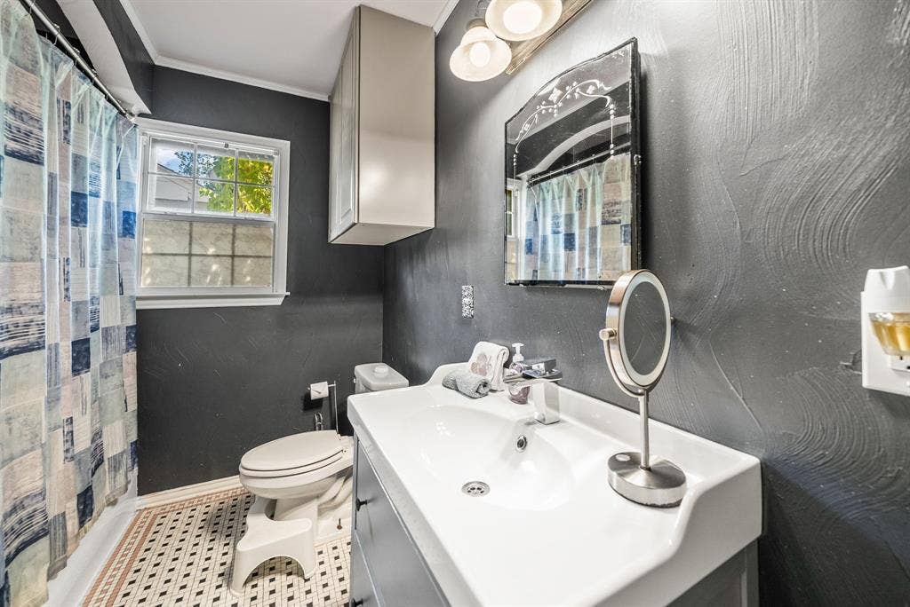 2807 Cain Boulevard, Dallas, TX 75211 Bathroom featuring a single vanity with integrated sink, wall-mounted cabinetry, a window with privacy glass, and patterned floor tiling