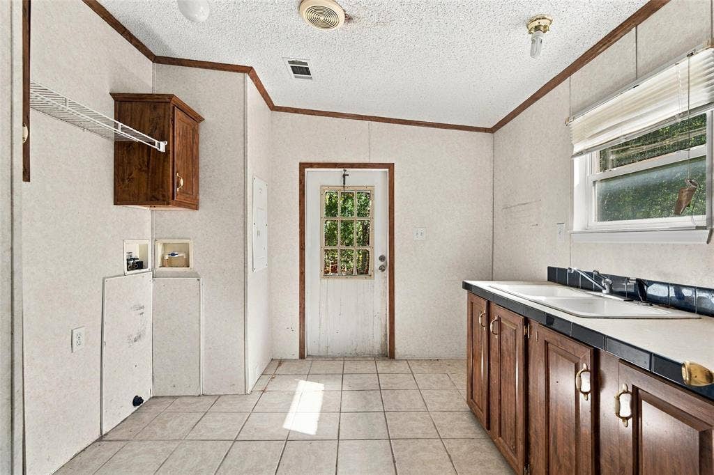 Utility area featuring tile flooring, wood-finish cabinetry, a dual-basin sink with a tile backsplash, and a six-panel exterior door with a glass inset