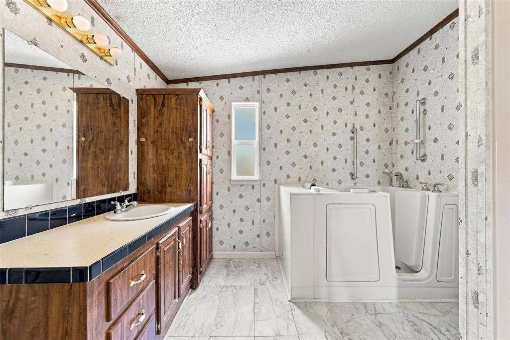 Bathroom featuring a walk-in tub with integrated safety bars, wood-finish cabinetry, a large wall-mounted mirror, and tile flooring