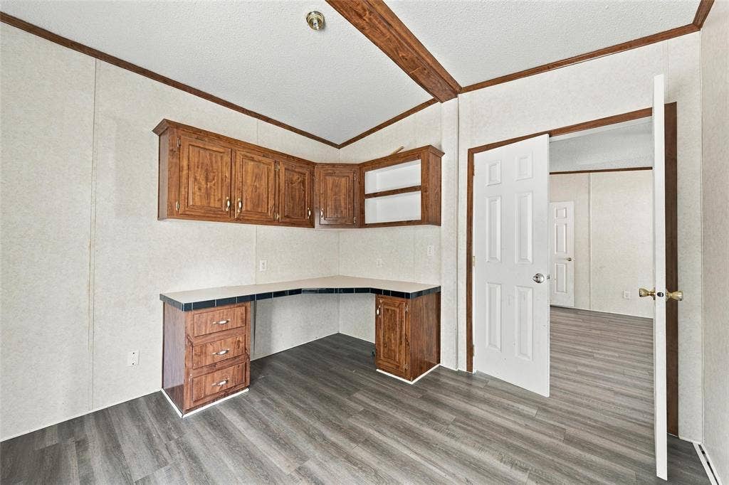 Built-in L-shaped desk with wood cabinetry, tiled countertop, multiple storage drawers, and matching overhead cabinets featuring wood-finish ceiling trim