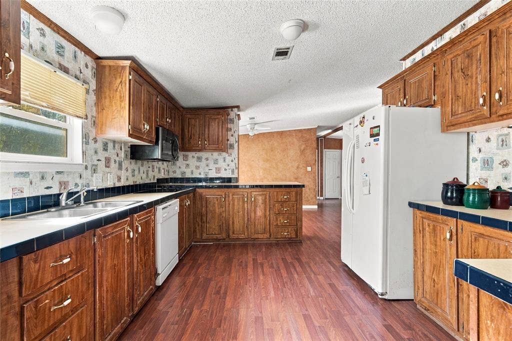 Kitchen featuring stained wood cabinetry, wood-finish flooring, dual-basin stainless steel sink, tile countertops, and built-in microwave