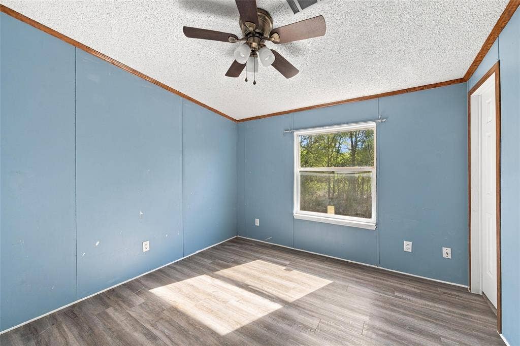 Wood-finish flooring, ceiling fan with integrated light fixture, single-pane window, and wood-trim crown molding