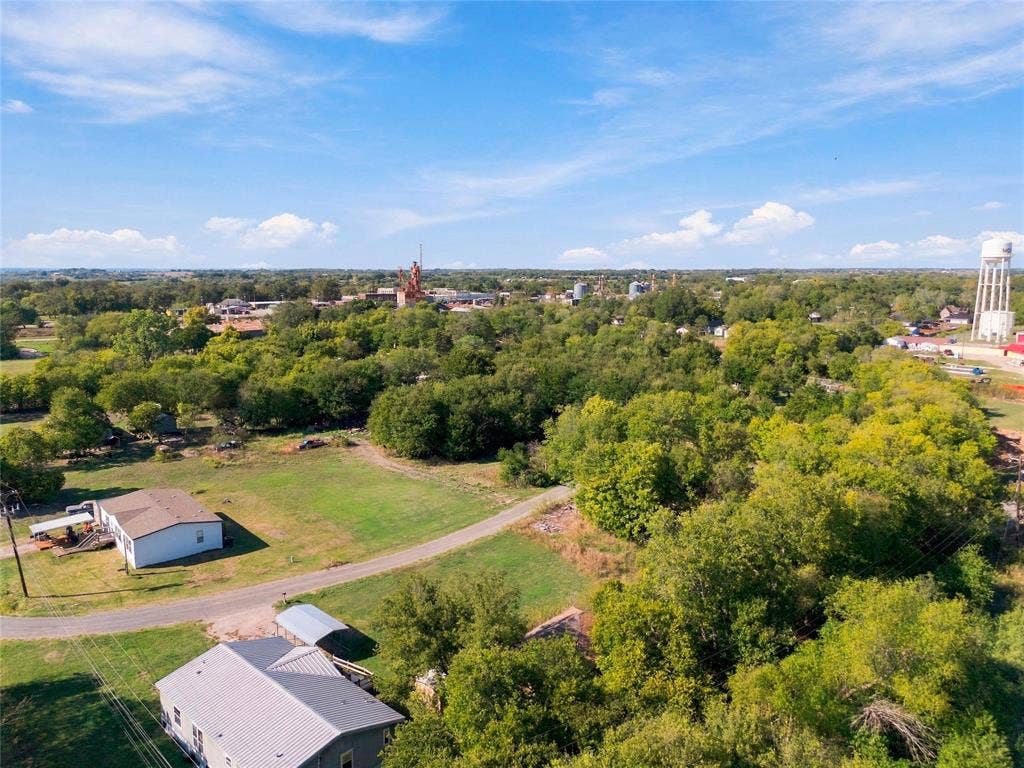 Aerial perspective featuring expansive acreage, mature tree clusters, open grass fields, and established road access
