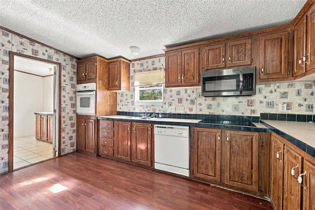 Kitchen featuring wood cabinetry, integrated wall oven, microwave, dishwasher, and wood-finish flooring