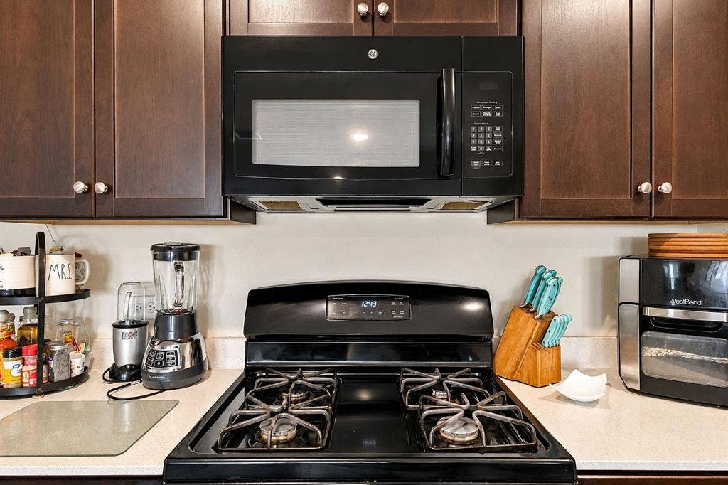 1516 Stonefield Drive, Anna, TX 75409 Dark-finish cabinetry paired with a black gas range and integrated over-the-range microwave, complemented by neutral-toned countertops