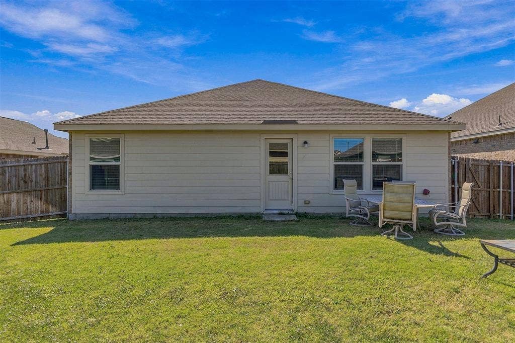 1516 Stonefield Drive, Anna, TX 75409 Rear exterior featuring horizontal siding, a hipped roof with asphalt shingles, double-pane windows, and a privacy wood fence