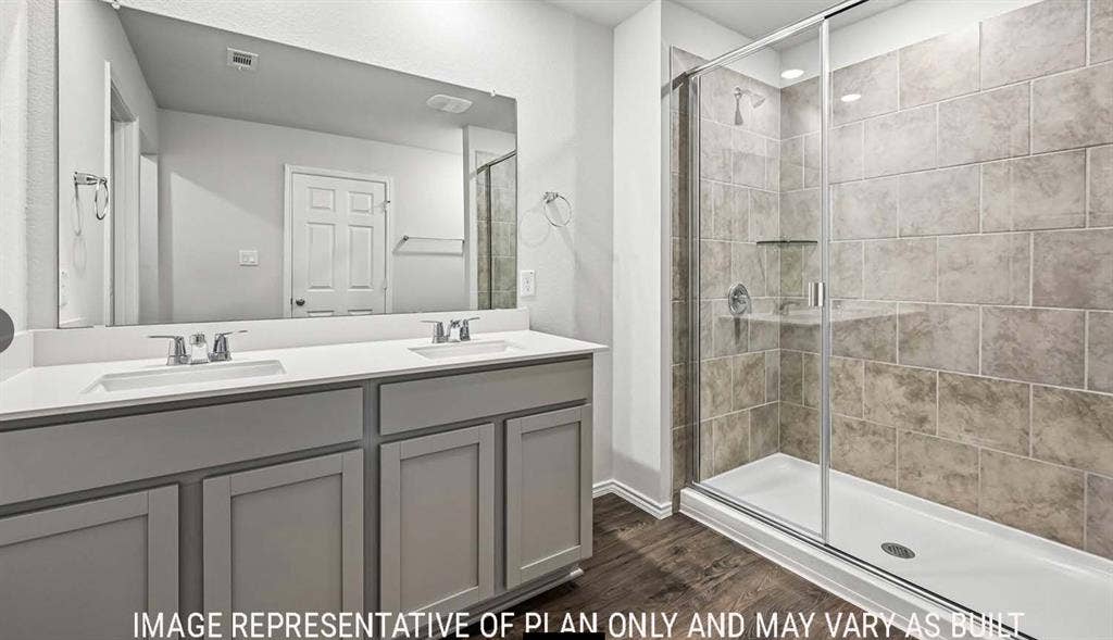 11813 Ceres Street, Lorena, TX 76655 Dual-sink vanity with neutral cabinetry, large wall-to-wall mirror, walk-in shower with tile surround, glass enclosure, and wood-finish flooring