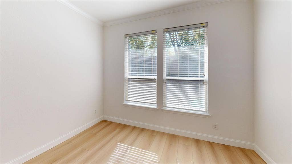 2254 Ash Grove Way, Dallas, TX 75228 Neutral-toned interior space featuring light wood-finish flooring, crown molding, and dual windows equipped with horizontal blinds