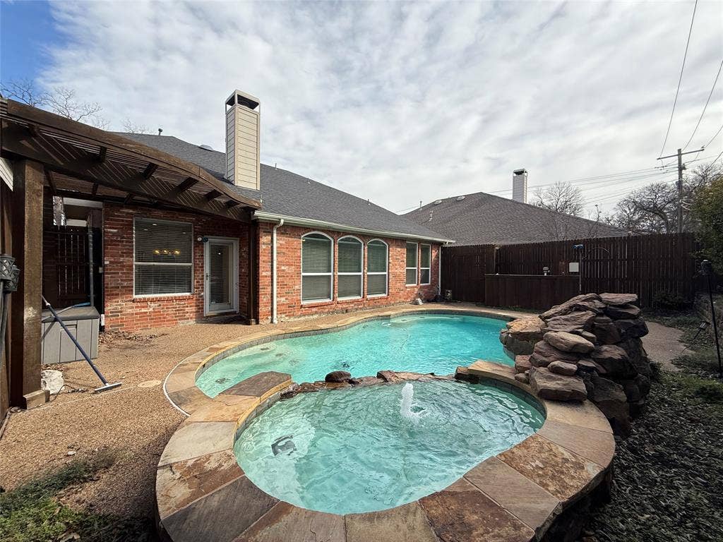 2254 Ash Grove Way, Dallas, TX 75228 Brick exterior featuring a swimming pool, attached spa with water feature, stone rock formation, and covered patio area