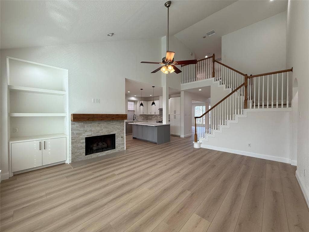 2254 Ash Grove Way, Dallas, TX 75228 Vaulted ceilings, wood-finish flooring, built-in cabinetry, stone-surround fireplace with a wooden mantel, and staircase with white railings