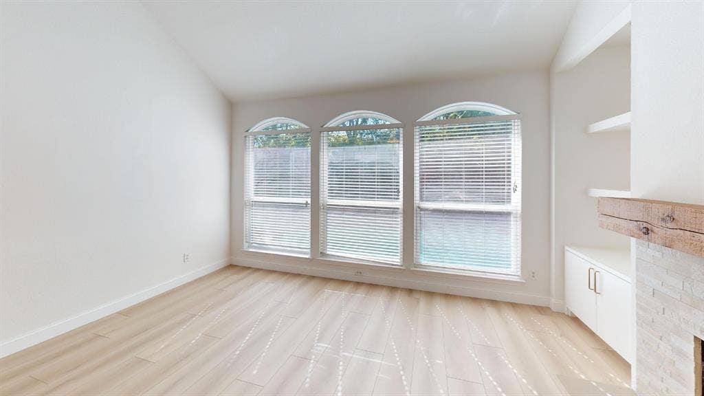 2254 Ash Grove Way, Dallas, TX 75228 Vaulted ceiling, wood-finish flooring, three arched windows, built-in cabinetry with shelving, and a stone-accented fireplace with a wood mantel