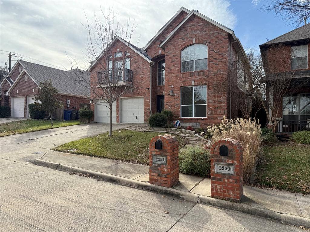 2254 Ash Grove Way, Dallas, TX 75228 Two-story brick exterior featuring a multi-gabled roofline, an integrated two-car garage, an upper-level balcony, and matching brick mailbox pillars