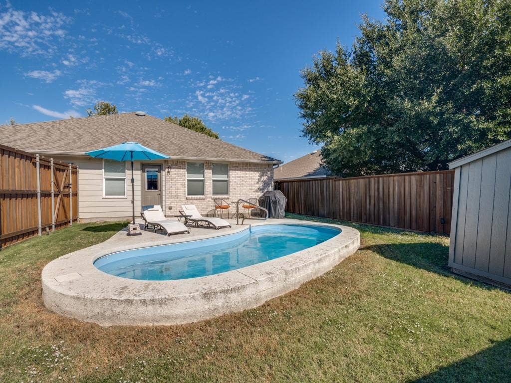 1728 Harvest Crossing Drive, Wylie, TX 75098 Oval-shaped swimming pool with concrete decking, enclosed by a full-height wood privacy fence and featuring an exterior storage shed