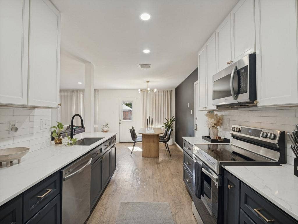 1728 Harvest Crossing Drive, Wylie, TX 75098 Kitchen featuring two-tone shaker cabinetry, light-toned stone countertops, white subway tile backsplash, stainless steel appliances, and wood-finish flooring
