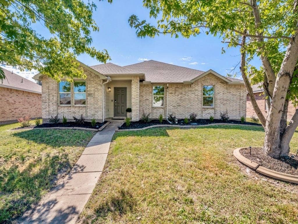 1728 Harvest Crossing Drive, Wylie, TX 75098 Single-story exterior featuring light-toned brick masonry, a concrete walkway, and landscaped garden beds with mature trees