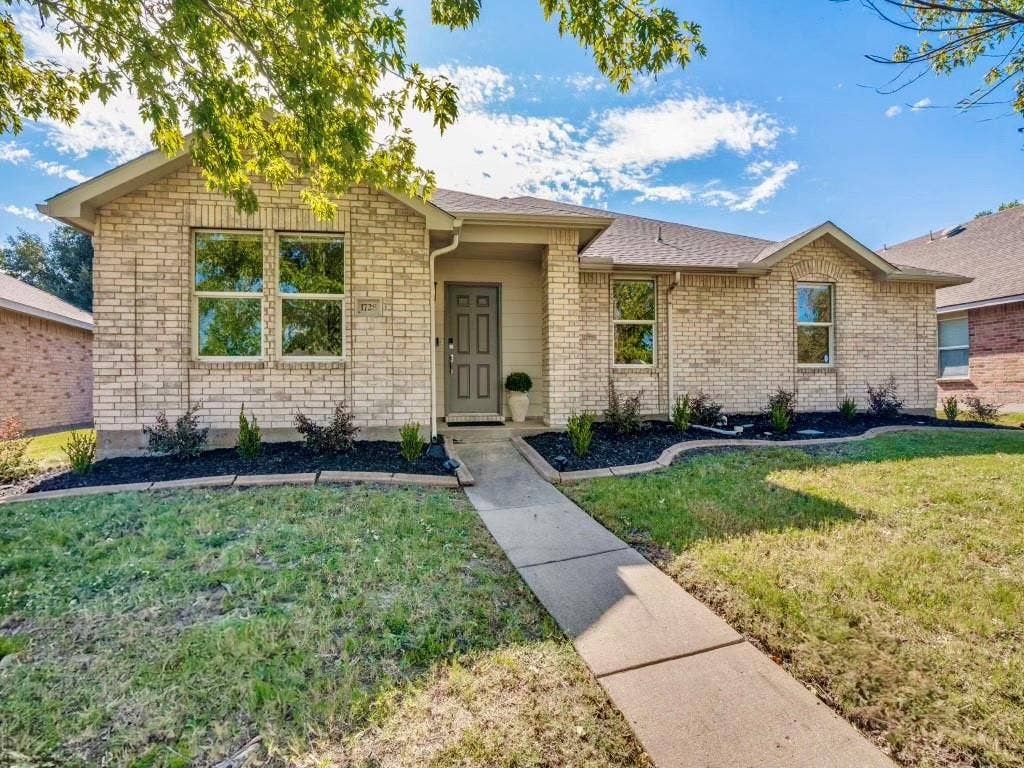 1728 Harvest Crossing Drive, Wylie, TX 75098 Single-story brick exterior featuring a multi-gabled roofline, concrete walkway, and landscaped garden beds with stone edging