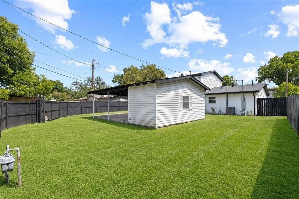Backyard featuring a manicured lawn, a detached white-sided structure with a covered patio, and perimeter wood fencing