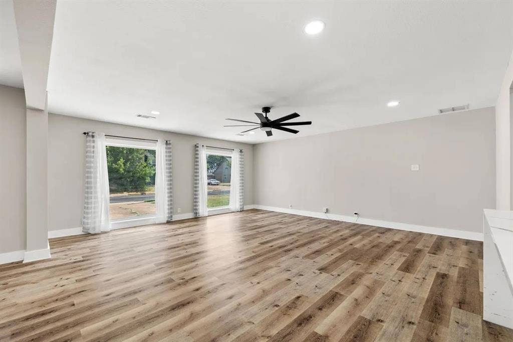 Open-concept interior featuring wood-finish flooring, recessed lighting, a matte black multi-blade ceiling fan, and dual energy-efficient windows