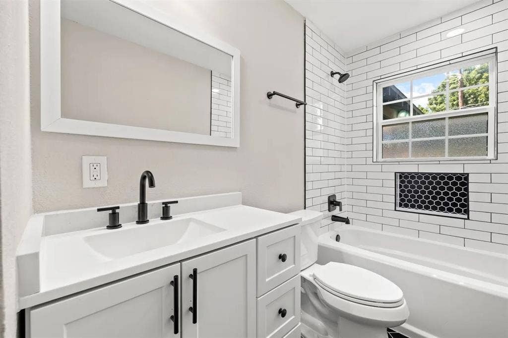 Bathroom featuring a vanity with a solid-surface countertop, subway tile shower surround with a decorative hexagonal inset, matte black fixtures, and a framed mirror