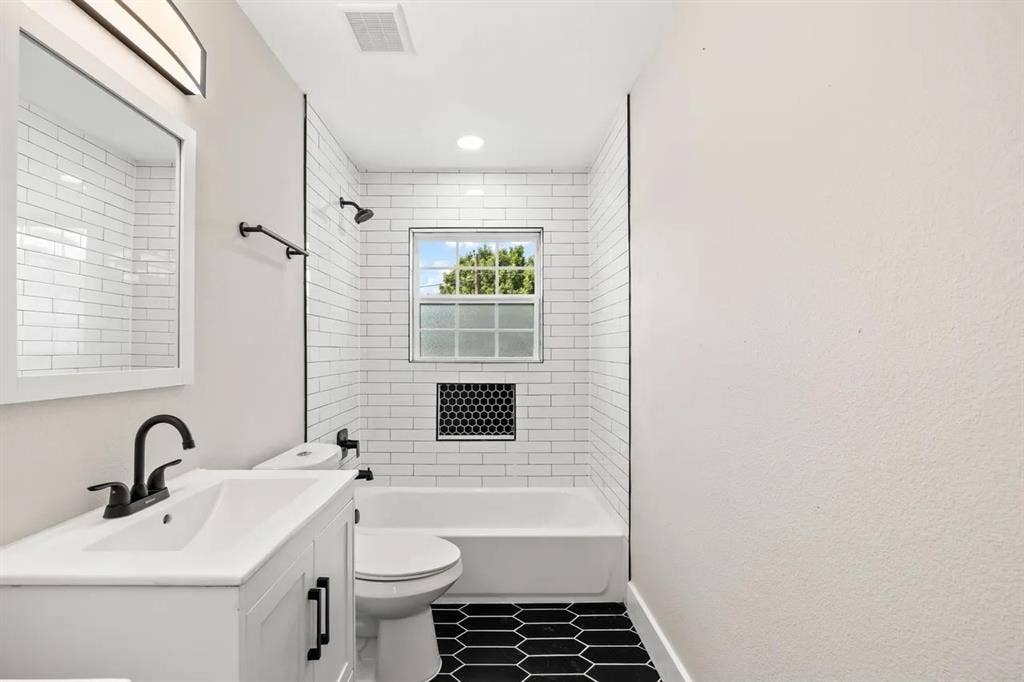 Bathroom featuring a white vanity with a rectangular sink, matte black faucet, subway-tiled tub surround with a built-in hexagonal niche, and black hexagonal floor tiling