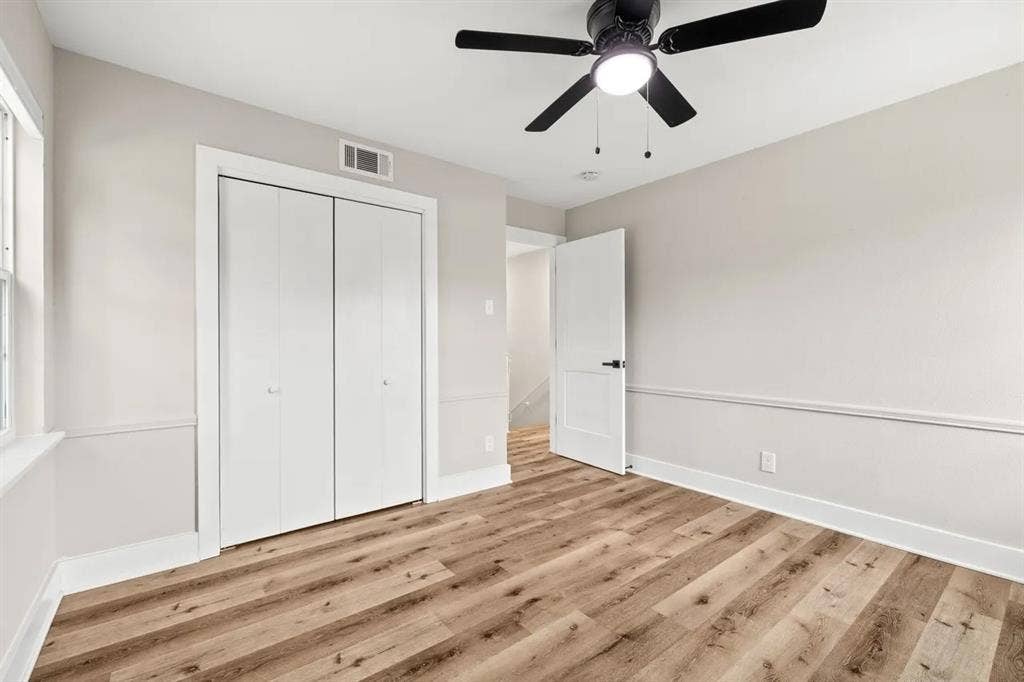 Room featuring wood-finish flooring, neutral wall paint, chair rail molding, a double-door closet, and a ceiling fan with integrated lighting
