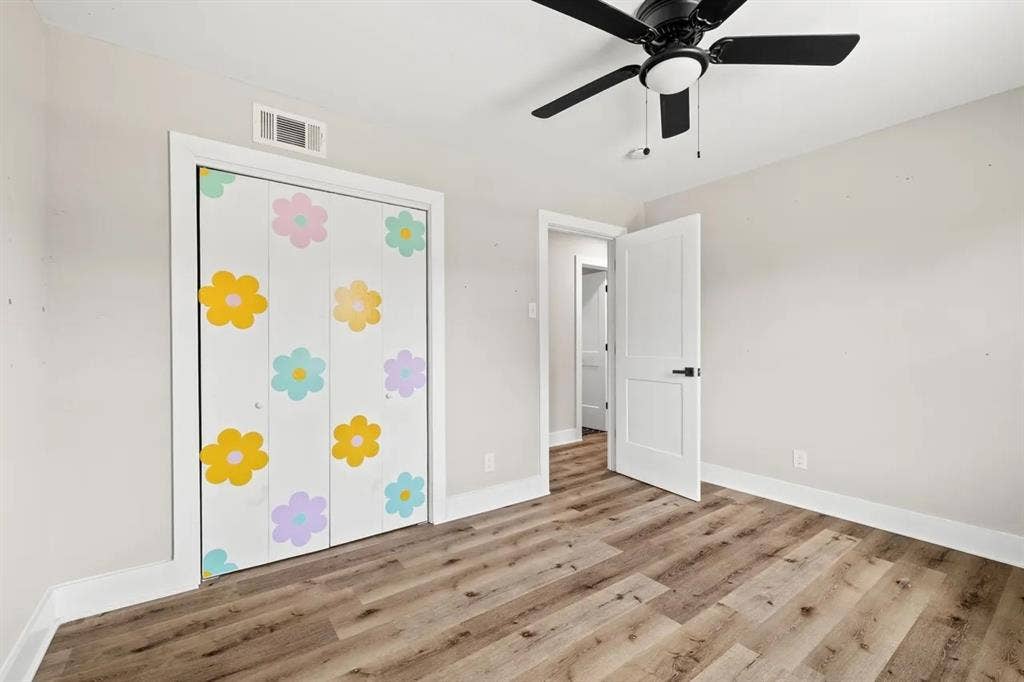 Wood-finish flooring, multi-panel interior door with matte black hardware, and a ceiling-mounted fan with integrated light fixture