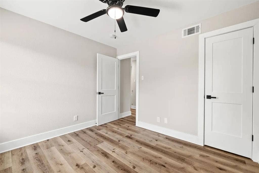 Wood-finish flooring, two-panel interior doors with matte black hardware, and a ceiling fan with integrated lighting