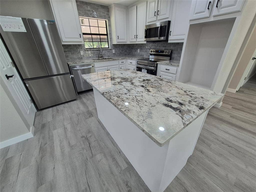 2029 Roberts Drive, Granbury, TX 76048 Kitchen featuring an island with stone-finish countertops, white cabinetry, stainless steel appliances, and wood-finish flooring