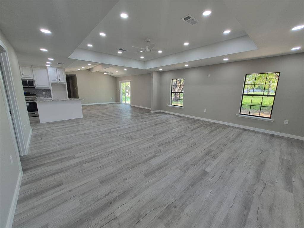 2029 Roberts Drive, Granbury, TX 76048 Open-concept space featuring wood-finish flooring, tray ceilings with recessed lighting, multi-pane windows, and a kitchen island with stone-surface countertop